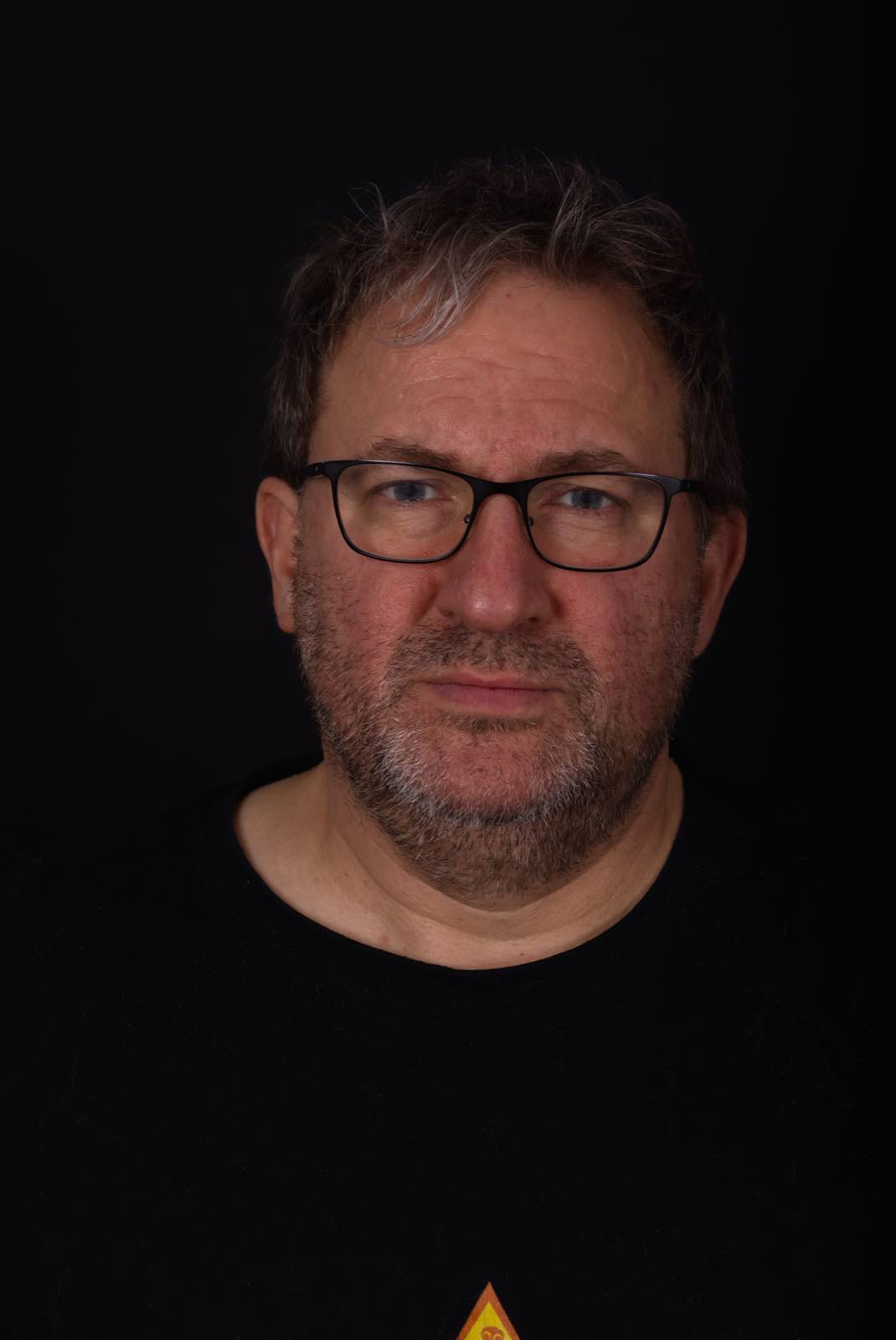 Charaktervolles Studio Portrait von Marcus mit Brille vor schwarzem Hintergrund
